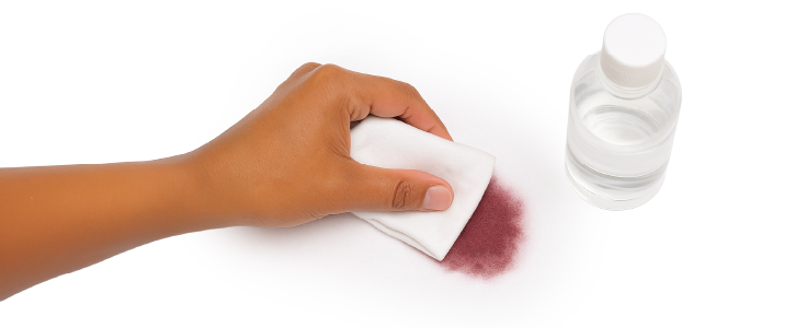 Mano limpiando mancha de tinte en ropa con paño blanco