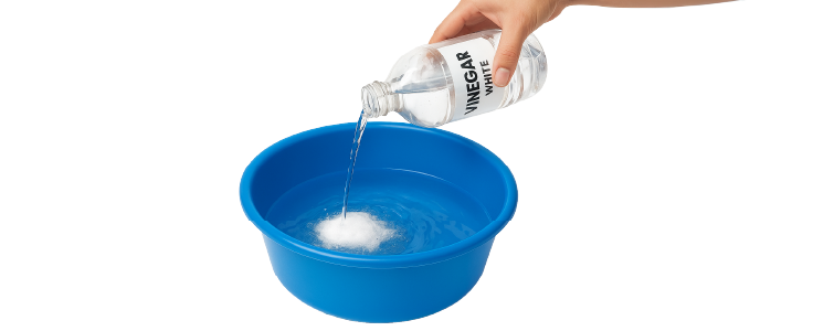 Mano vertiendo vinagre blanco en una cubeta con agua y bicarbonato de sodio